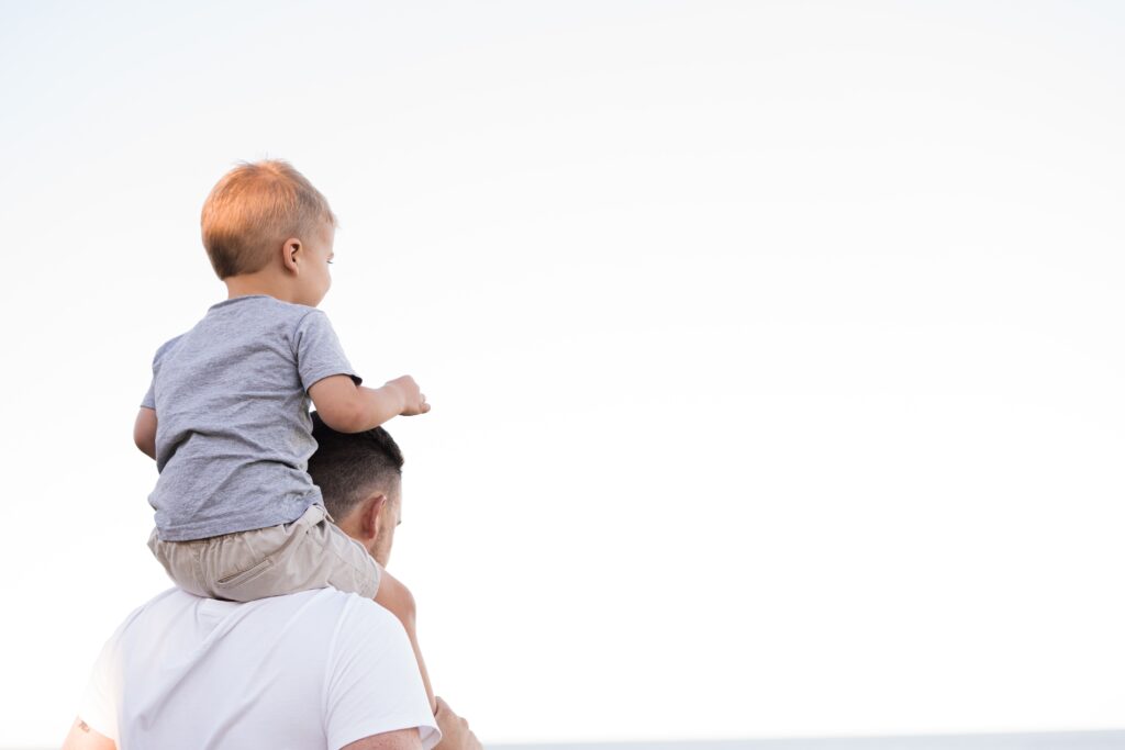 A boy toddler sitting atop his father’s shoulders